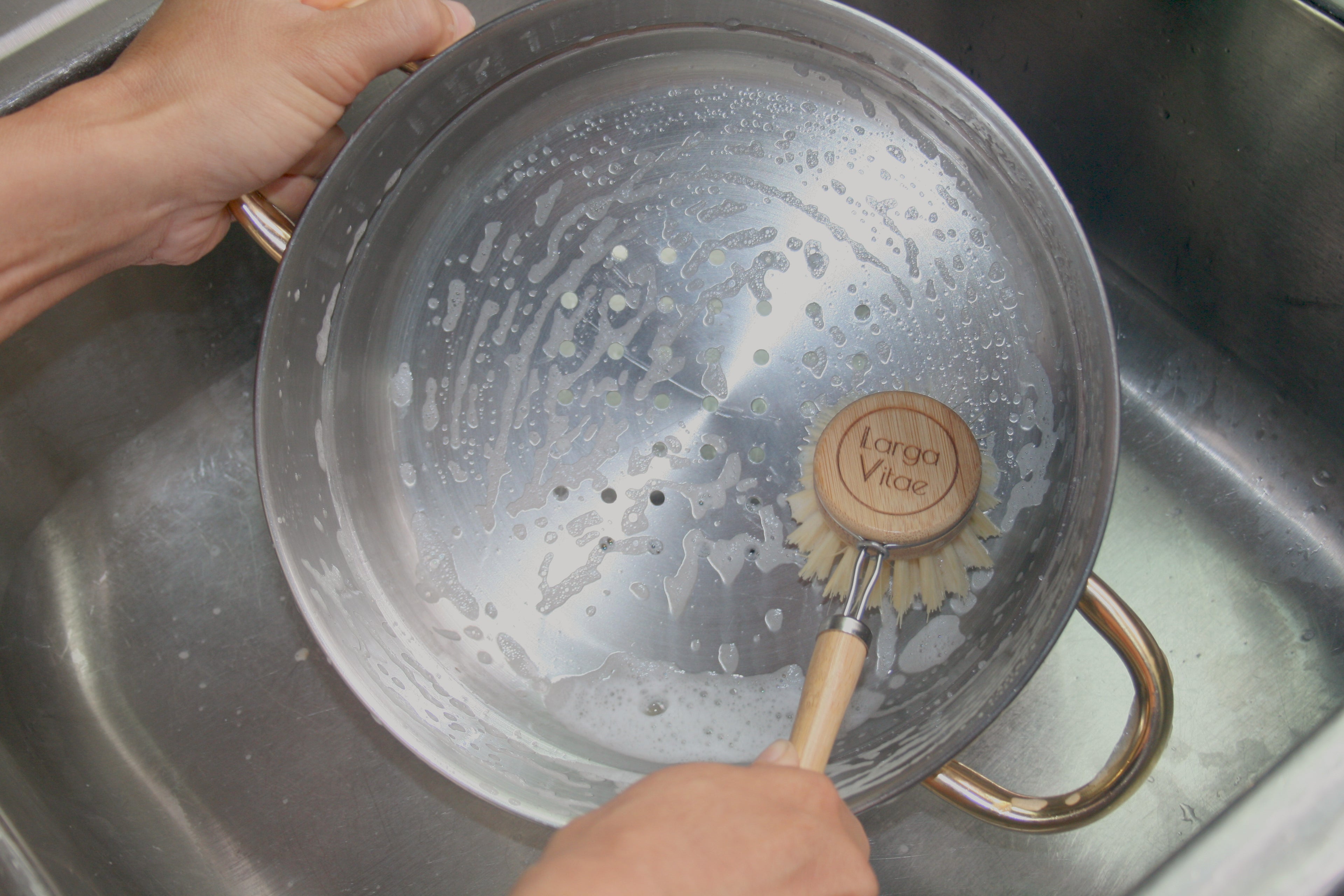 Person scrubbing a pot with a sustainable wooden dish scrubber in a sink