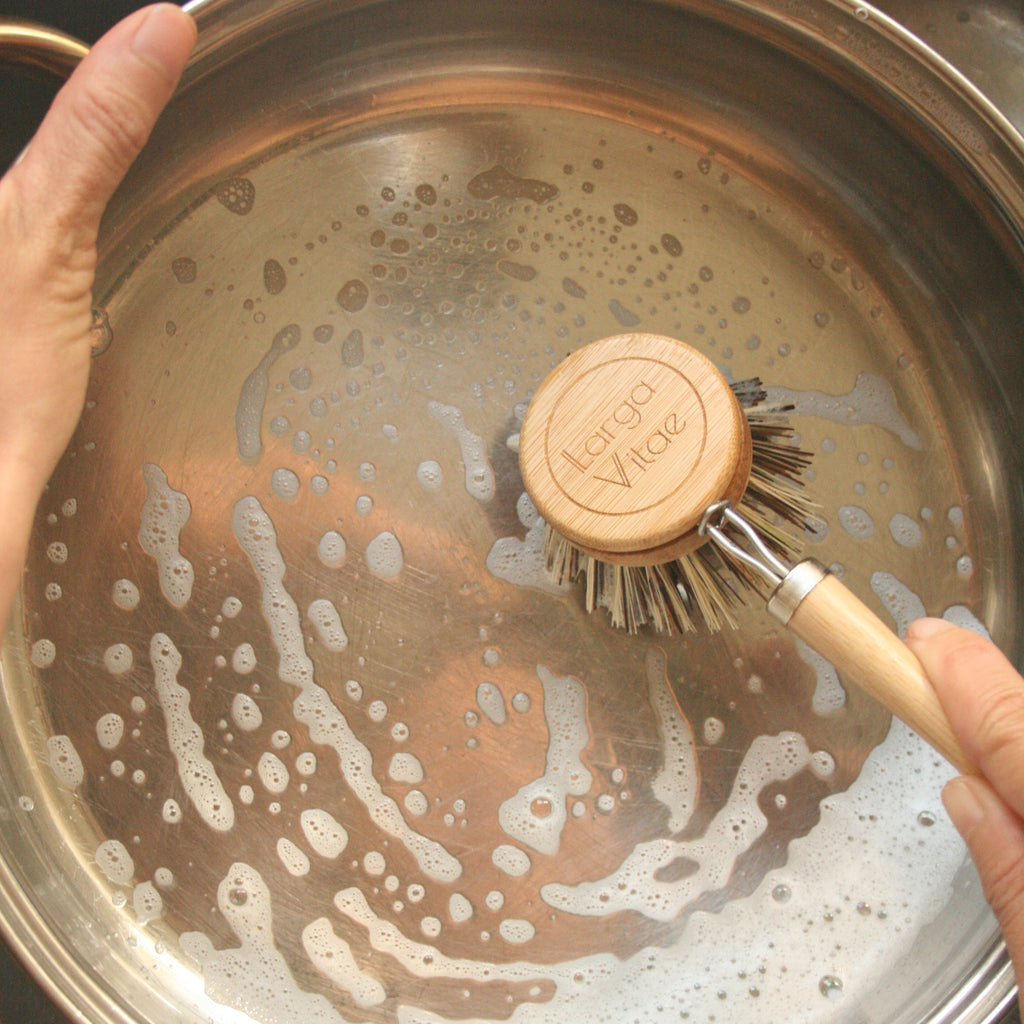 Person scrubbing a pot with a sustainable wood scrubber in a sink