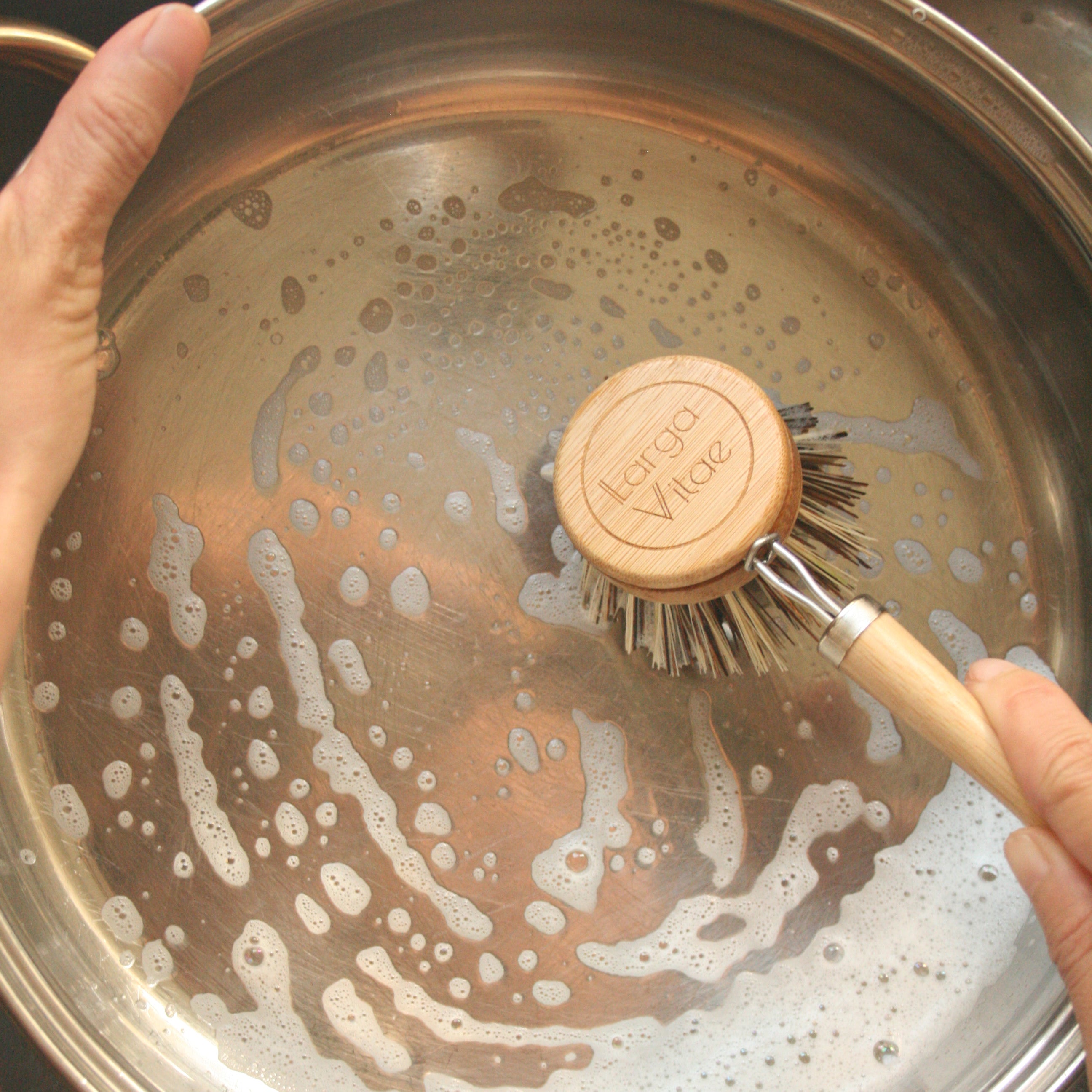 Person scrubbing a pot with a sustainable wood scrubber in a sink