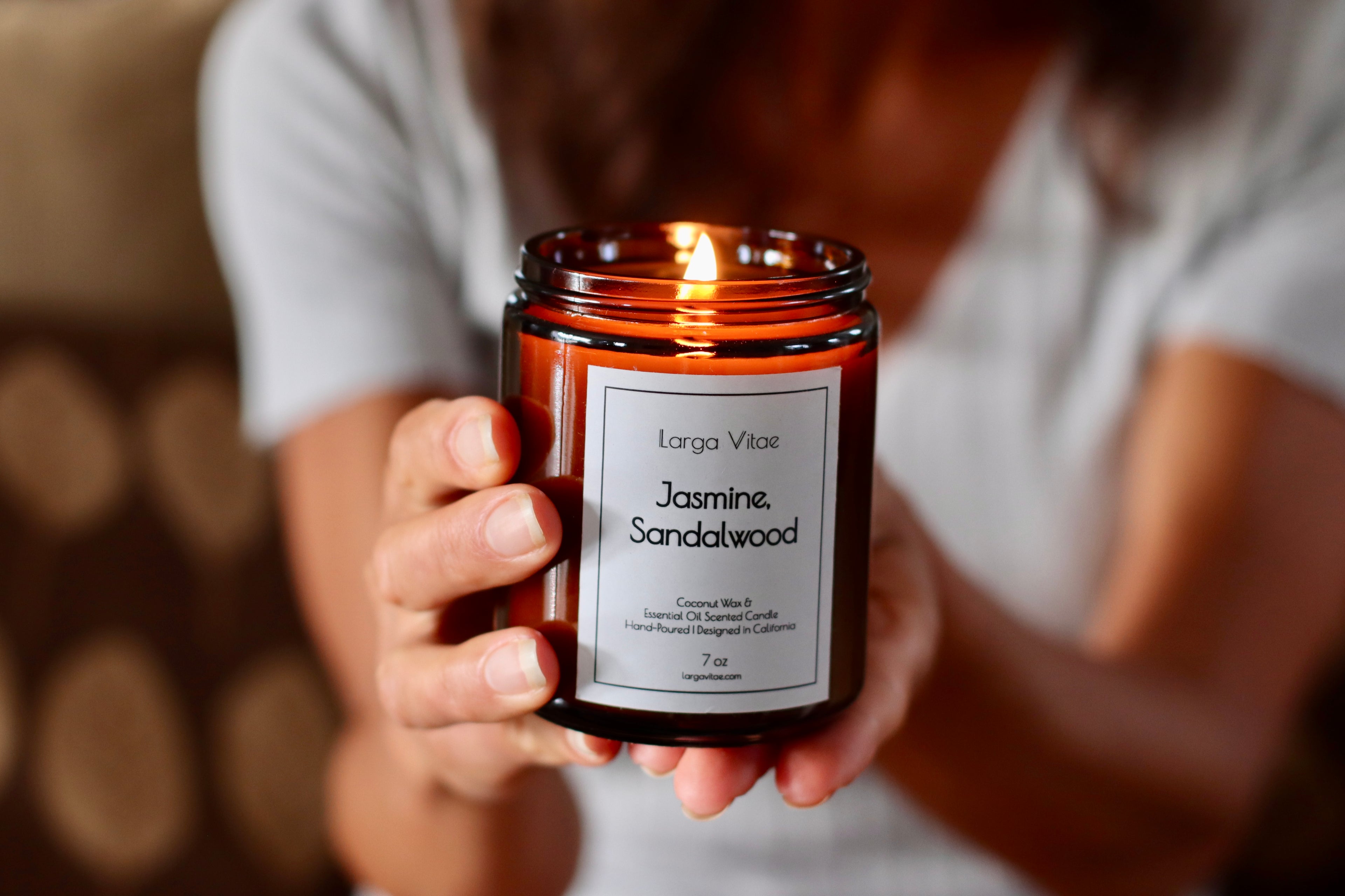 Woman holding a romantically lit Larga Vitae Jasmine Sandalwood candle with a blurred background