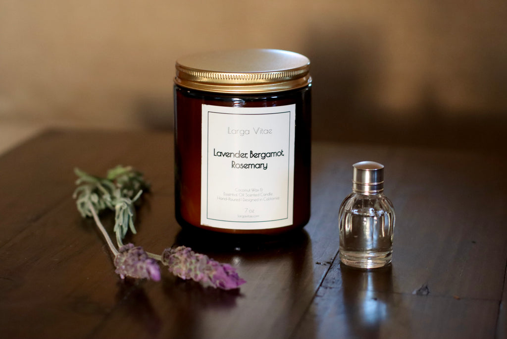 Jar of Lavender Bergamot Rosemary candle with a small bottle of essential oil and lavender sprigs on a wooden surface.
