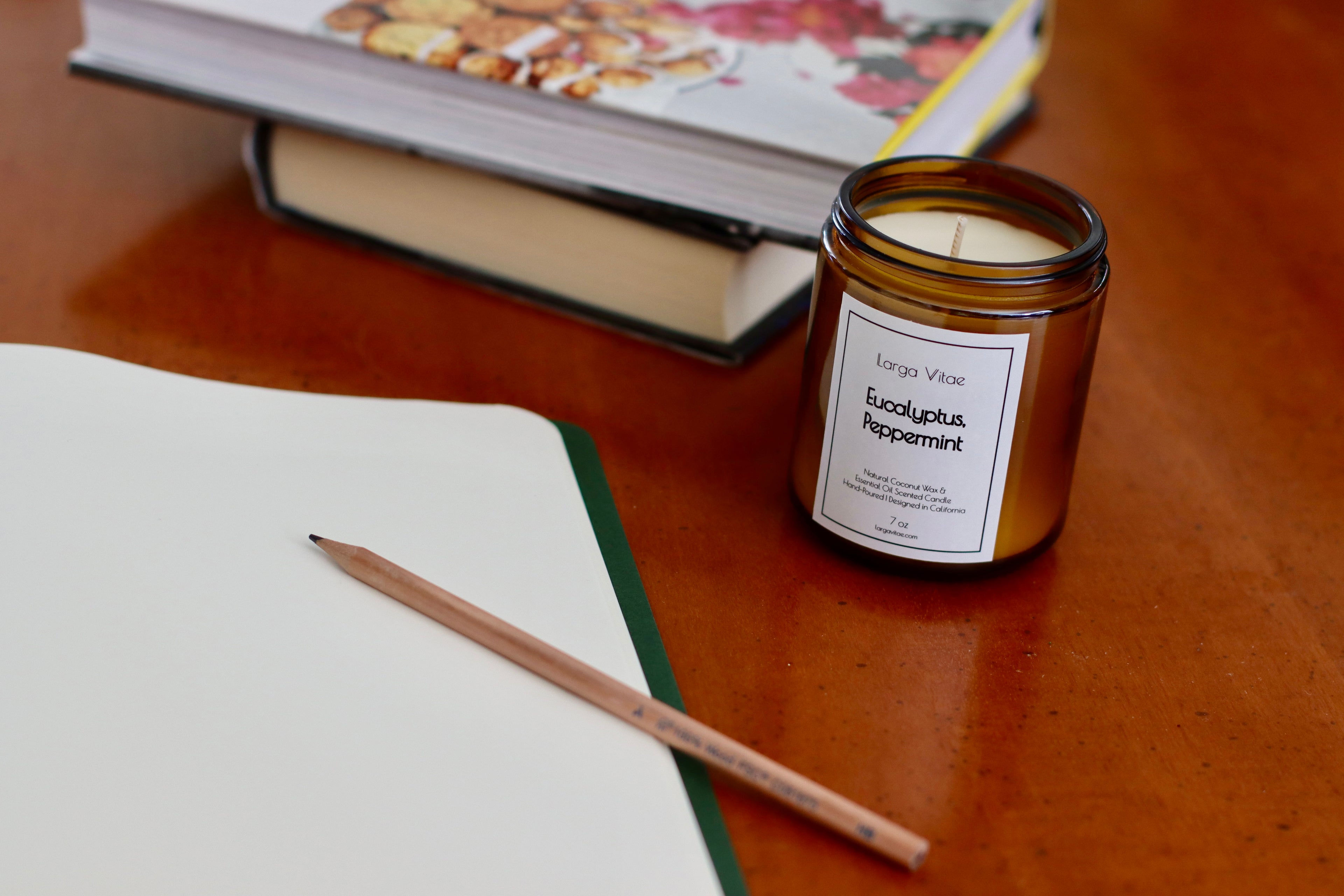 Larga Vitae's mint candle on a wooden surface next to a notebook and pencil