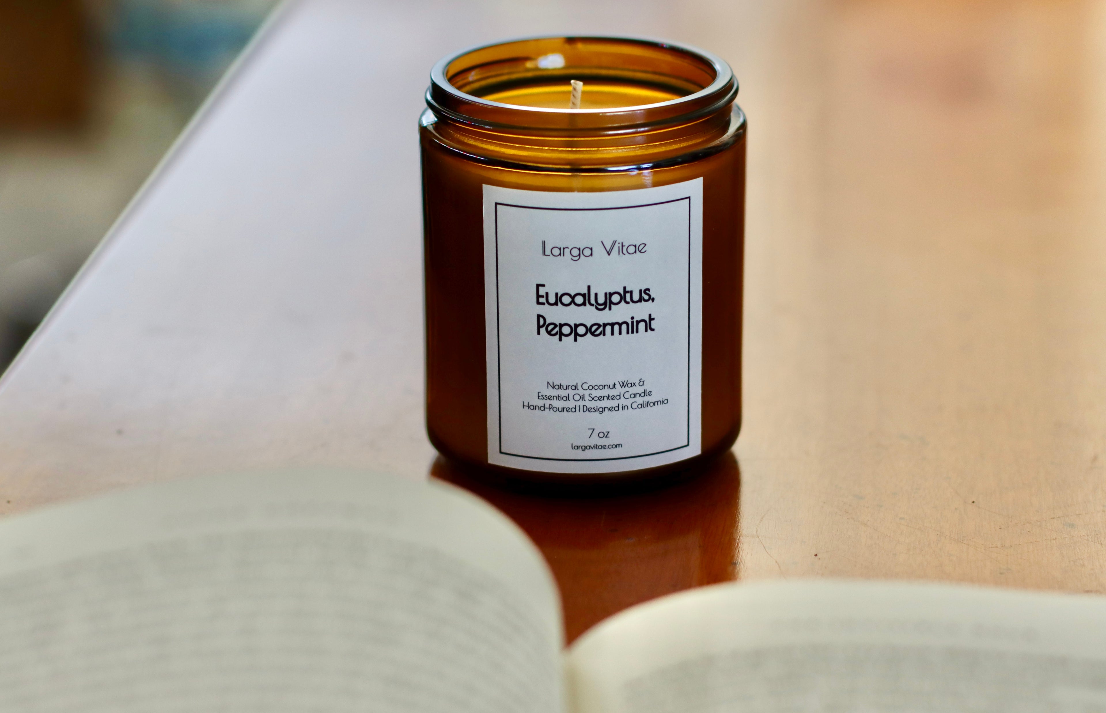 Larga Vitae's amber glass candle jar labeled 'Eucalyptus Peppermint' on a wood surface with an open book in the foreground