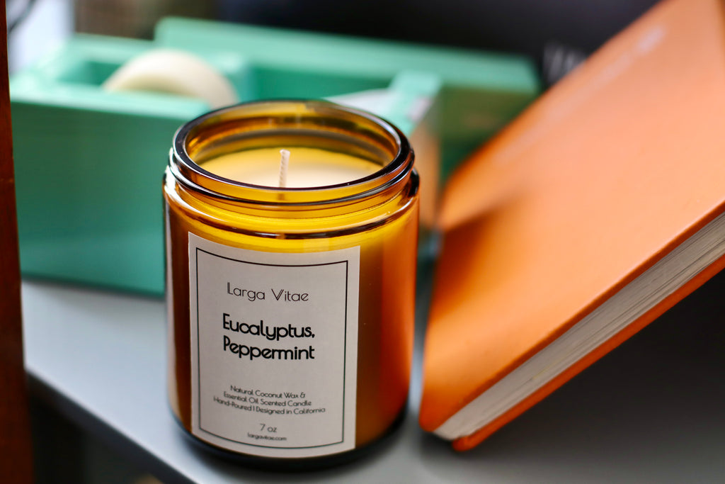 Eucalyptus Peppermint naturally scented candle by Larga Vitae on a surface with books in the background.