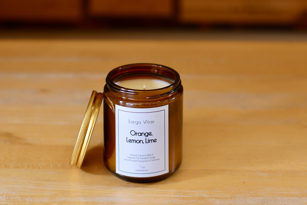 Larga Vitae's Orange, Lemon, Lime natural fragrance oil candle in a classy amber glass jar on a wooden surface